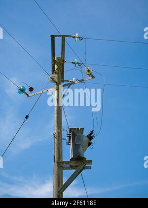 Eine dreiphasige 11kV-Stromleitung auf einem Holzmast und ein Abschalttransformator für eine 230V-Netz-Stromversorgung in Großbritannien. Stockfoto