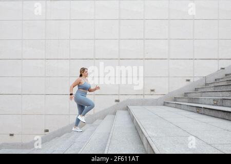 Determined fit plus size junge Frau läuft die Treppe im Freien, Training in der Stadt und das Erreichen des Zielkonzepts