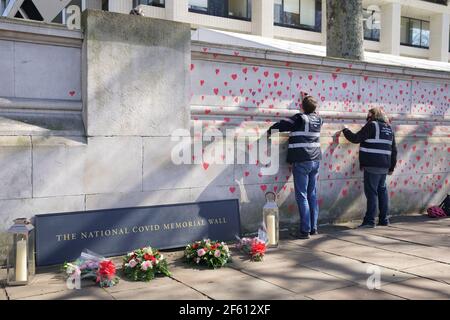 Menschen, die rote Herzen auf der COVID-19 Memorial Wall gegenüber dem Houses of Parliament in Embankment im Zentrum von London malen, um an die mehr als 145.000 Menschen zu erinnern, die in Großbritannien an dem Coronavirus gestorben sind. Bilddatum: Montag, 29. März 2021. Stockfoto