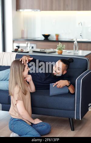Glücklich gut aussehende bärtige Mann in der Liebe auf dem Sofa liegen und Berührende Haare seiner hübschen Freundin mit zart Stockfoto