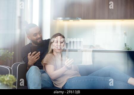 Ziemlich lächelnde junge Frau zeigt etwas Interessantes, das sie auf gefunden internet für Ehemann, wenn sie sich auf dem Sofa ausruhen Zu Hause Stockfoto