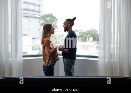 Glückliches gemischtes Paar in der Liebe, das auf dem Balkon steht, die Hände hält und einander anschaut Stockfoto