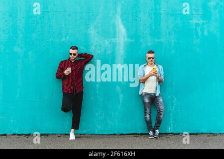 Paar Männer mit Handy vor einer blauen Wand Hintergrund - Konzept der Verliebtheit mit Technologie, soziale Netzwerke und Handy - LGBT Stockfoto