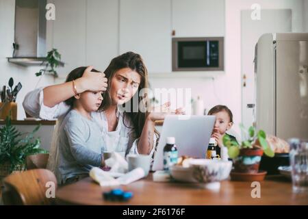 Mutter mit Kindern, die Online-Beratung über Videoanruf in Küche Stockfoto