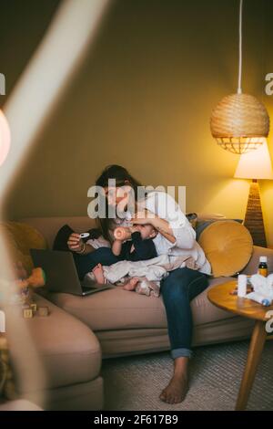 Mutter überprüft die Temperatur des kleinen Mädchens, während sie Rat eingibt Online-Beratung zu Hause während der COVID-19 Stockfoto