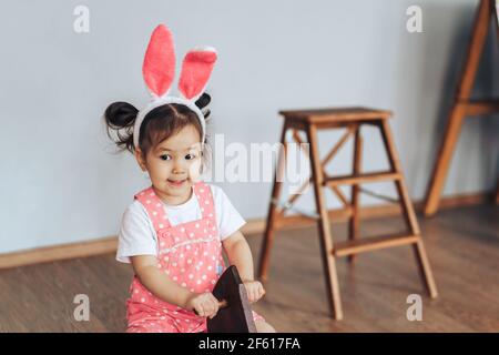 Asiatische Mädchen von zwei Jahren alt ist in roten Kleid mit weißen Tupfen gekleidet. Das Kind schwingt auf Pferdeschaukel. Das Kind hat Kaninchenohren auf dem Kopf. Th Stockfoto