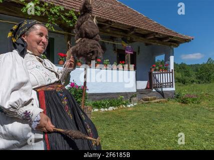 Salaj, Siebenbürgen, Rumänien-14. Mai 2018: Alte Frau in traditioneller rumänischer Volkstracht gekleidet, Spinnerei Wolle vor ihrem charmanten Haus Stockfoto