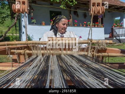 Salaj, Transsilvanien, Rumänien-14. Mai 2018: Alte Frau in traditioneller rumänischer Volkstracht, die an der alten Holzwebmaschine vor ihrem Saibling arbeitet Stockfoto