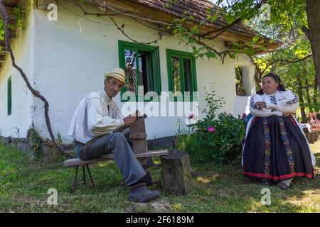 Salaj, Transsilvanien, Rumänien-14. Mai 2018: Altes Paar, Mann und Frau in traditioneller rumänischer Tracht, die vor ihrem charmanten Haus arbeiten Stockfoto