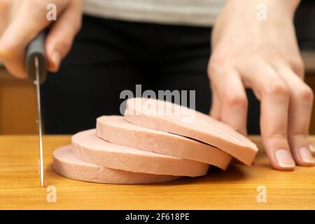 Die Hände der Frauen schneiden die gekochte Wurst in Kreise auf einem hölzernen Nahaufnahme des Boards Stockfoto