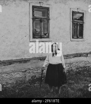 Salaj, Siebenbürgen, Rumänien-14. Mai 2018: Sehr alte Frau, die allein vor ihrem alten Haus auf dem Land steht. Schwarz und Weiß, Vintage-Stimmung Stockfoto