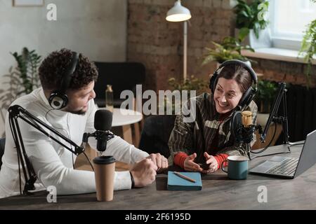 Mann und Frau sprechen miteinander, während sie sitzen Der Tisch mit Mikrofonen und die Arbeit am Radio Stockfoto