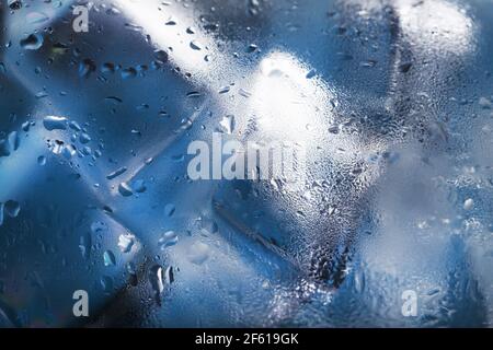 Eiswürfel in einem vernebelten Glas mit Tropfen Eiswasser Nahaufnahme Makro. Erfrischendes und kühlendes Getränk bei heißem Wetter. Blauer Hintergrund. Vollbild Stockfoto