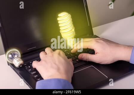 Hände auf einen Laptop und eine Glühbirne als Idee. Eine Idee ging aus, die zweite kam zur Inspiration. Das Konzept der regenerierenden Ideen. Stockfoto