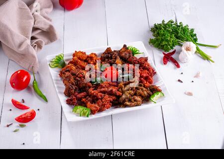 Chicken Pakoda oder Pakora, drei verschiedene Geschmacksrichtungen von Pakora angeordnet in Eine weiße quadratische Platte und garniert mit Tomaten und Gurken Auf weiße te gelegt Stockfoto