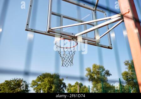 Nahaufnahme Basketballkorb gegen blauen Himmel im Stadtpark. Basketballplatz von hinten Zaun. Selektiver Fokus, unscharfer Hintergrund Stockfoto
