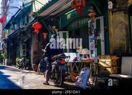 Ein Motorradfahrer hält an, um Essen in einem kleinen Restaurant in einer sonnenbeschienenen Gasse in Talat Noi, Bangkok, Thailand zu bestellen Stockfoto