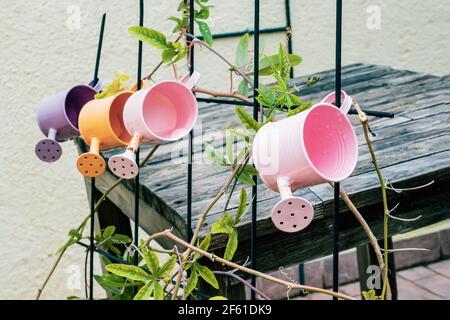 Gießkannen als Gestaltungselement. Bunte Gießkannen hängen als Dekoration des Sommergartens am Zaun. Alte Dinge in modernem Design. Stockfoto