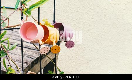 Gießkannen als Gestaltungselement. Bunte Gießkannen hängen als Dekoration des Sommergartens am Zaun. Alte Dinge in modernem Design. Stockfoto