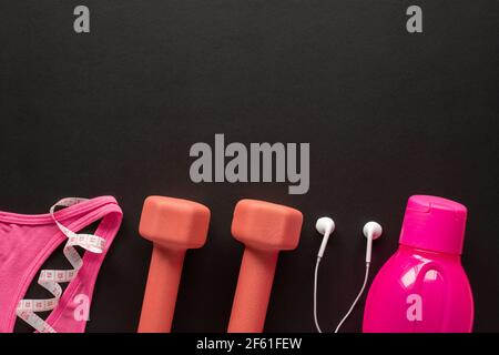 Kurzhanteln, Maßband, Wasserflasche, Kopfhörer und Sportbekleidung auf schwarzem Hintergrund. Fitness-, Sport- und Trainingskonzept Flat Lay mit Kopierfläche. Stockfoto