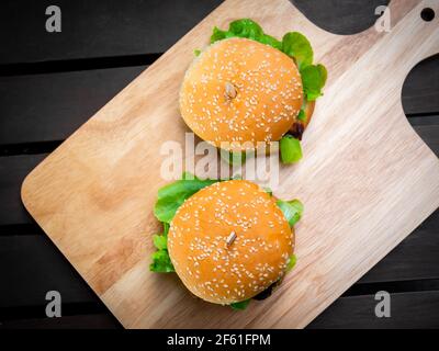 Köstliche frische hausgemachte Burger Blick von oben. Zwei leckere hausgemachte Hamburger auf Holztablett oder Holz Schneidebrett auf dunklem Hintergrund. Stockfoto