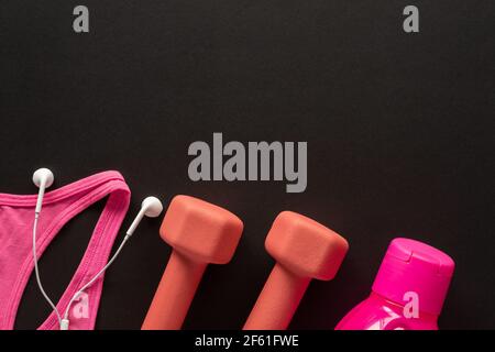 Kurzhanteln, Wasserflasche, Kopfhörer und Sportbekleidung auf schwarzem Hintergrund. Fitness-, Sport- und Trainingskonzept Flat Lay mit Kopierfläche. Stockfoto