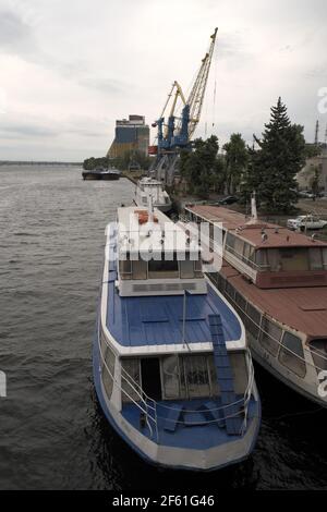 Flusskreuzfahrtschiff, der neben dem Kai festgemacht ist, mit Kräne dahinter, Fluss Dnepr, Dnipro, Ukraine. Stockfoto