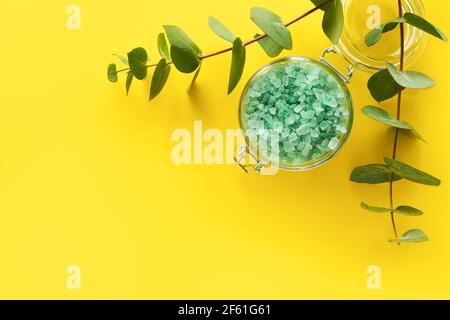 Eukalyptus-Badesalz und Zweige von frischem Eukalyptus auf gelbem Hintergrund. SPA, Körperpflege-Konzept. Platz für Text kopieren, Draufsicht. Stockfoto