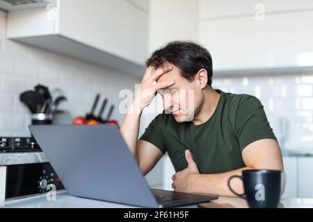 Troubled junge kaukasischen Mann sitzen in der Küche Blick auf Laptop-Bildschirm denken Nachdenken über Problemlösung, nachdenkliche männliche Freiberufler Arbeit am Computer, ma Stockfoto