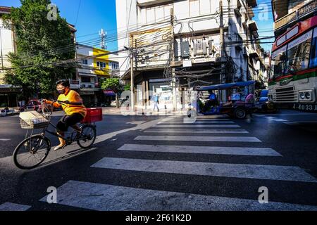 Eine ältere Frau radelt über eine Fußgängerüberfahrt in Talat Noi, Bangkok, Thailand Stockfoto