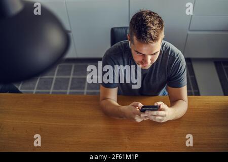 Das digitale Zeitalter. Ein Blick aus der Vogelperspektive auf einen jungen Mann, der in Blau am Küchentisch sitzt und seine Zeit plant und organisiert. Erstellen von To-Do-Listen Organisieren Stockfoto