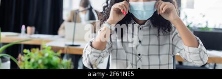 Teilansicht der afroamerikanischen Geschäftsfrau Anpassung medizinische Maske im Büro, Banner Stockfoto