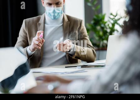 Geschäftsmann in medizinische Maske Anwendung Hand Desinfektionsmittel auf verschwommenem Vordergrund Stockfoto