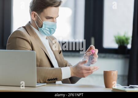 Geschäftsmann in Schutzmaske Anwendung Handdesinfektionsmittel am Arbeitsplatz Stockfoto