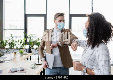 Interracial Geschäftspartner in medizinischen Masken tun Ellbogen Gruß in Büro Stockfoto