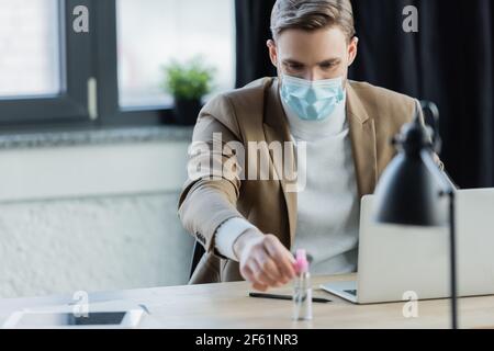 Junge Geschäftsmann in medizinische Maske unter antiseptischen während sitzen Arbeitsplatz Stockfoto