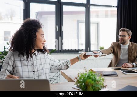 afroamerikanische Geschäftsfrau, die Kollegen auf unscharfem Hintergrund Papiere gibt Stockfoto