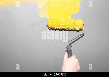 Renovierung im Haus. Eine Frau malt eine graue Wand mit einer Walze in ein gelbes Leuchtlicht. Veränderung im Leben. Positive Stimmung. Kopieren Sie den Speicherplatz in das lef Stockfoto