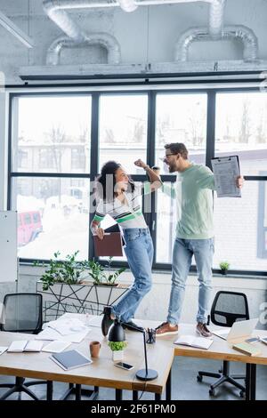 Aufgeregt interracial Geschäftsleute mit Papieren und zum Mitnehmen Getränk stehen Auf dem Tisch Stockfoto