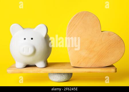 Sparschwein und Holzherz auf Teeteboard vor farbigem Hintergrund. Konzept des Gleichgewichts Stockfoto