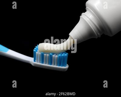 Zahnpasta wird aus der Tube auf eine blaue Zahnbürste gepresst, isoliert auf schwarzem Hintergrund Stockfoto