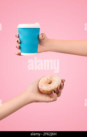 Womans Hände halten bunte Donut und Kaffeetasse auf rosa Hintergrund. Stockfoto