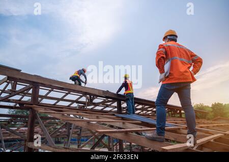 Ingenieur Techniker beobachten Team von Dachdecker arbeiten auf Dachkonstruktion des Gebäudes auf der Baustelle, Dach Metallblech Konstruktion Konzept. Stockfoto