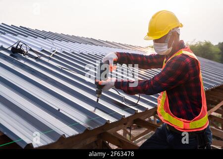 Sicherheitsverschleiß der Bauarbeiter mit elektrischen Bohrwerkzeugen installieren auf neuem Dachblech, Dachkonstruktion Konzept. Stockfoto