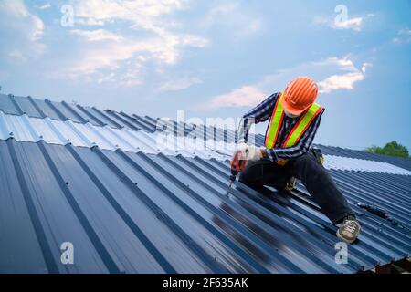Asian Dachdecker Arbeitsschutz tragen mit Luft oder pneumatische Nagelpistole und Installation auf neue Dach-Blech, Dachkonzept von Wohngebäude unter con Stockfoto