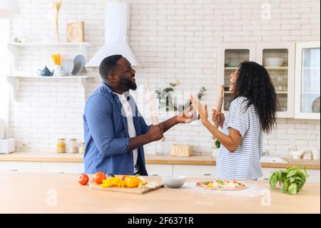 Glücklich fröhlich schwarzen Ehepaar Mann und Frau Spaß haben singen in der Küche, Kochen zusammen zu Hause. Überglücklich junges Paar in der Liebe Vorbereitung Mahlzeit gesundes Essen, genießen aktive Familie Wochenende Stockfoto