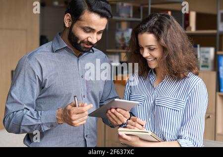 Indische und hispanische glückliche Kollegen sprechen mit digitalen Tablet im Büro. Stockfoto