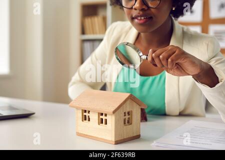 Immobilienmakler mit einer Lupe Blick auf ein Kleines Haus auf ihrem Tisch Stockfoto