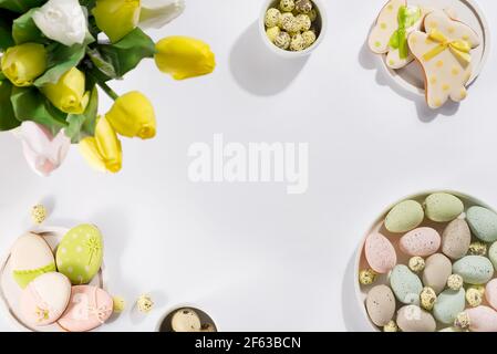 Ostertisch-Setting mit einem Teller aus farbigen Pastelleiern, einem Bouquet aus Tulpen und Keksen in Form von Kaninchen auf hellem Hintergrund Stockfoto