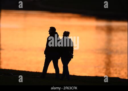 Dresden, Deutschland. März 2021, 29th. Zwei Menschen schilhouettierten am Ufer der Elbe bei Sonnenuntergang. Quelle: Sebastian Kahnert/dpa-Zentralbild/dpa/Alamy Live News Stockfoto